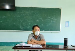 A person wearing a mask in front of a chalkboardDescription automatically generated