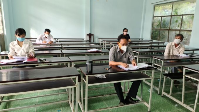 A person wearing a mask sitting at a desk in a classroomDescription automatically generated